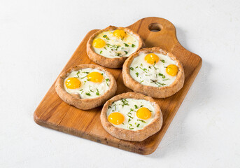 Small open pies with mozzarella, quail eggs and dill, on a wooden board. Light background