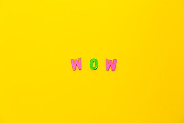The word wow made from toy plastic letters pink and green colors on a yellow background. Symbol of happy emotion. Something amazing. Exclamation fraze. Success