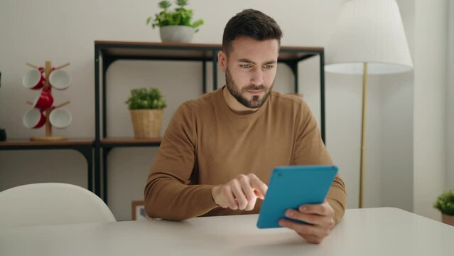 Young hispanic man using touchpad sitting on table at home