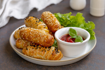 Mini hot dog bites. Freshly baked puff pastry rolls or buns with filling served on a plate with...
