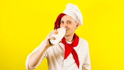 Man with red dreadlocks with bottle milk. Confident young cook in white shirt and red tie drinks milk from a bottle against yellow background