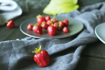 Fresh strawberries on a plate, against the background of green leaves and gray linen fabric 