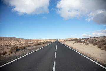 Einsame gerade Straße in einer öden Landschaft auf Fuerteventura. Sonniger Himmel mit schönen...