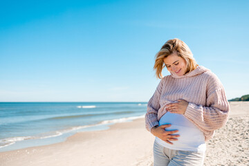 Happy beautiful pregnant woman walking on sandy beach