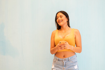 Joven guapa  de pelo largo con camiseta amarillo, posando con un teléfono sobre un aislado...
