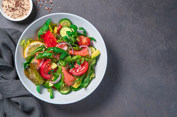 Salad with salmon, vegetables and fresh herbs on a dark background.