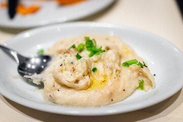 Closeup of restaurant table for Thanksgiving dinner and macro texture of mashed potatoes on white plate with spoon, oil, black pepper and green onion