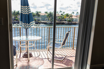 Glass table and railing nobody on balcony terrace and blue umbrella outside in Hollywood Beach, north of Miami, Florida with chairs and view of waterway river with luxury houses across
