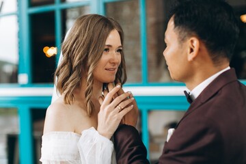 Wedding day. Beautiful European bride and her Asian groom posing against the backdrop of cafes and large windows.