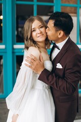 Wedding day. Beautiful European bride and her Asian groom posing against the backdrop of cafes and large windows.