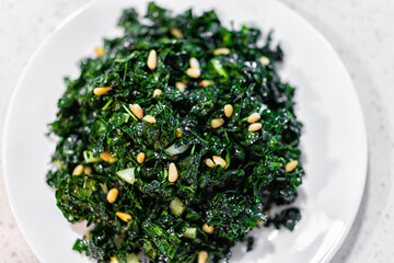 Flat top closeup texture view of green kale vegan vegetarian salad on white plate with pine nuts and olive oil background - obrazy, fototapety, plakaty