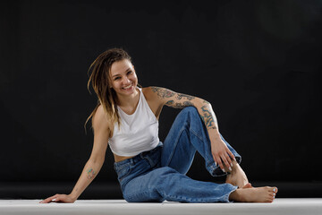 Fototapeta na wymiar tattooed girl in jeans and a white tank top on a black background