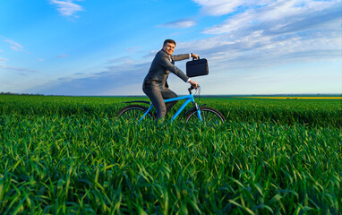 businessman rides a bicycle through a green grass field, dressed in a business suit, he has a briefcase and documents, beautiful nature in spring, business concept