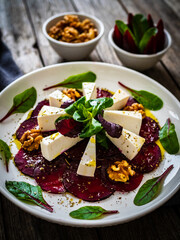 Beetroot carpaccio with goat cheese, greens and walnuts on wooden background
