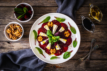 Beetroot carpaccio with goat cheese, greens and walnuts on wooden background
