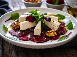 Beetroot carpaccio with goat cheese, greens and walnuts on wooden background
