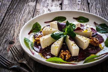 Beetroot carpaccio with goat cheese, greens and walnuts on wooden background
