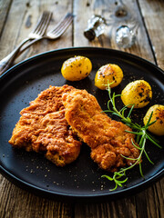 Breaded fried pork chop with potatoes and rosemary  on wooden table
