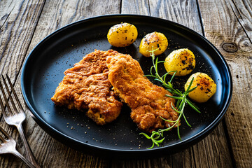 Breaded fried pork chop with potatoes and rosemary  on wooden table
