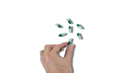 Fingers of a hand picking up a group of green pharmacy capsules