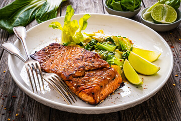 Fried teriyaki salmon steak with pak choi and lime on wooden table
