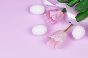 Easter holiday background with white chicken eggs and pink tulip flowers on pink background. Congratulatory Easter background with copy space.