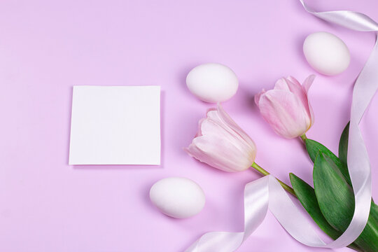 Easter greeting card with white eggs and pink tulip flowers over pink background. Top view flat lay with image copy space.