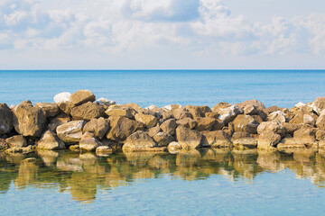 Stone breakwater rocks are reflected in the water - image with copy space on sky