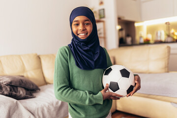 Muslim girl posing at home with football ball.