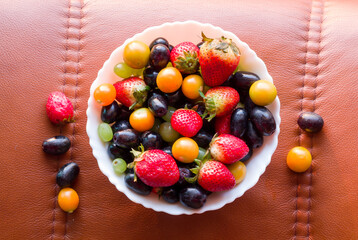 Top view of bowl containing mix of fresh,juicy,sweet cape gooseberries,grapes and strawberries. The fruit bowl is isolated on a dark rustic background.