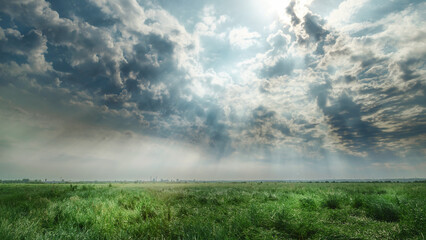 Dramatic cloudy sky over green field with sun rays