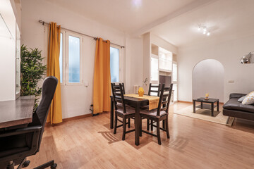 Living room with dark wood dining table and matching chairs with yellow accents to match curtains, wooden desk and black office chai