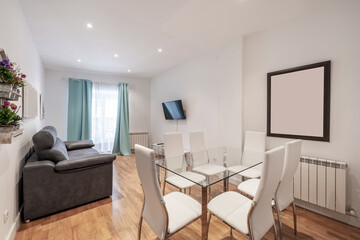 Living room with glass dining table with white upholstered chairs, white wood and glass doors, wall-mounted TV and gray leather two-seater sofa and French oak parquet floor