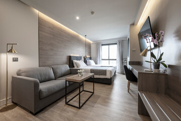 Hotel room with double beds, upholstered sofa bed, large window with curtains and wooden flooring