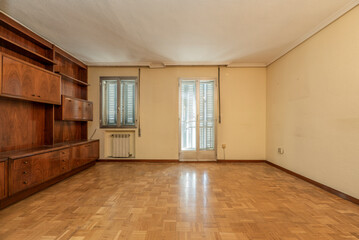 Obraz premium Wooden mural bookcase room, aluminum window and exit doors to covered terrace with radiator grill, cream-colored painted walls and plaster molding on the ceiling