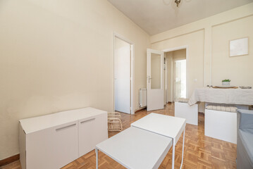 Living room with dining table with tablecloth, gray two-seater sofa, coffee tables, white woodwork, cream-colored walls and parquet floors