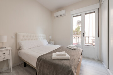 Fototapeta na wymiar Double bed with courtesy blanket and towels, air conditioning and balcony with white aluminum doors