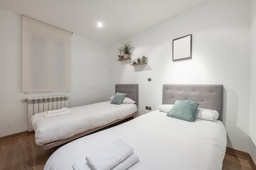 bedroom with two separate beds with upholstered headboards, wooden shelves with decorative plants, blind window, white aluminum radiator and towels in a vacation rental apartment