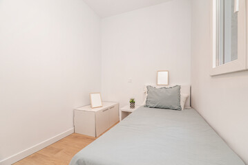 Youth bedroom with small bed with blue bedspread, white aluminum window and matching bedside table