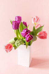 Bouquet of pink and purple tulips with colorful quail eggs over pink background. Mother's day holiday concept.