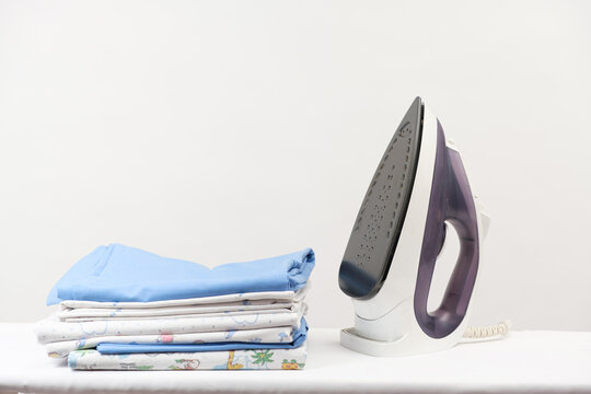 Iron and a stack of ironed clothes and baby diapers on a white background with space for text.