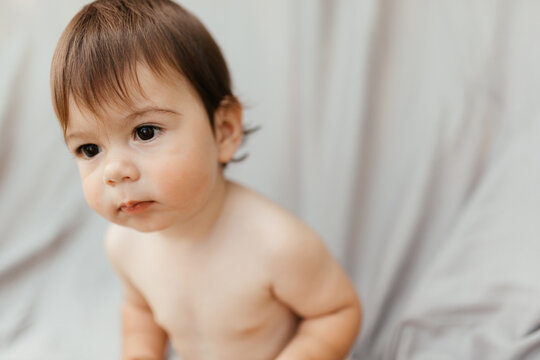 A baby in a diaper sits on the street on a gray background and looks away