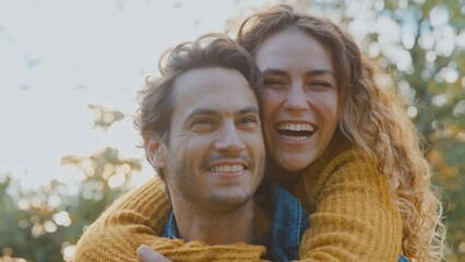 Portrait of happy loving couple with man giving woman piggyback and hugging her in autumn park - shot in slow motion  - Powered by Adobe