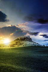 Fototapeta na wymiar day and night time change concept above the castle on the hill. composite fantasy landscape. grassy meadow in the foreground. rocky peaks of the ridge in the distant background with sun and moon
