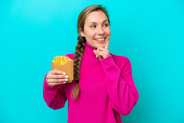Young caucasian woman holding fried chips isolated on blue background thinking an idea while looking up