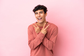 Young Argentinian man isolated on pink background smiling and showing victory sign