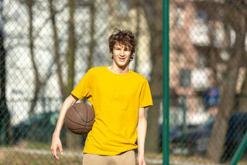 Cute young teenager in yellow t shirt with a ball plays basketball. Sports, hobby, active lifestyle for boys