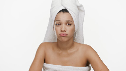 Funny African American woman with a towel on her head performs disappointed facial expression on white background