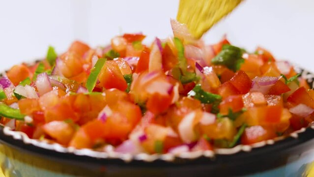 Pico de Gallo close up. Hand dipping tortilla chip into plate of traditional pico de gallo. Bowl of tasty Pico de Gallo salsa and nachos chips. Mexican food concept