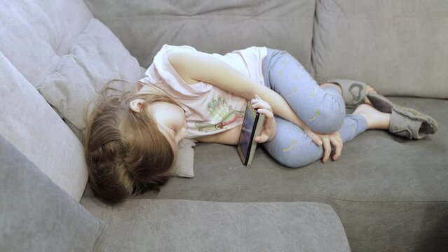 a little girl is lying on the couch and watching cartoons on the phone screen